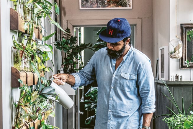 Hilton Carter tending watering a living wall of plants in his apartment hallway